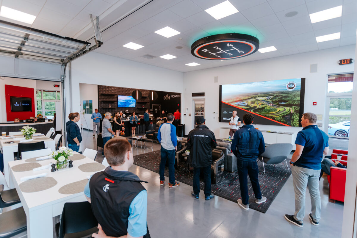 The interior of the Club House Lounge with a group of people listening to a man speaking